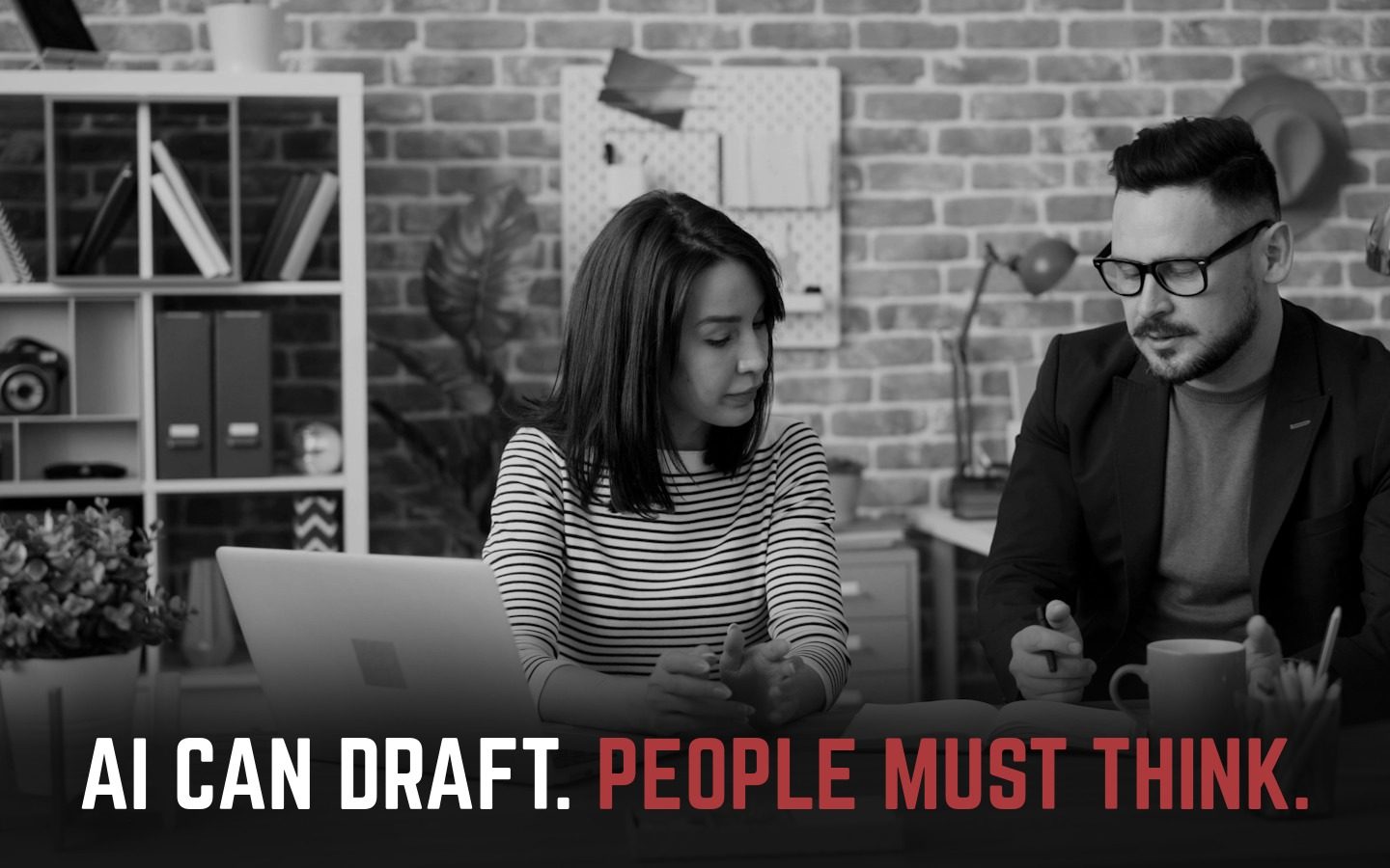 Two colleagues discussing notes beside a laptop. AI can draft. People must think.